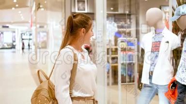 4k视频：微笑的年轻女子在大型购物中心橱窗或橱窗后寻找新时尚服装